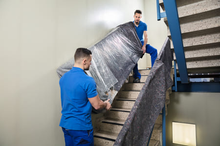 movers in blue uniforms carry a couch down a flight of stairs
