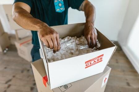 a mover places a fragile item into a cardboard box filled with packing peanuts