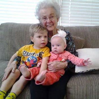 A grandma is sitting on a couch holding two young grandchildren