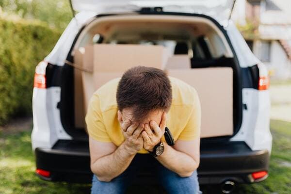 man stressed and covering face with hands near car trunk
