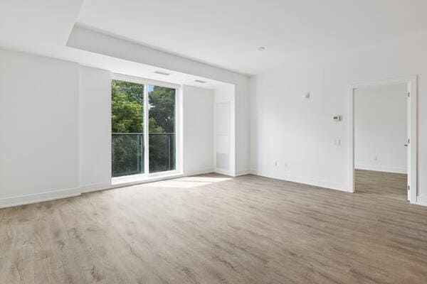 An empty apartment with white walls, light wood floors, and a sliding glass door