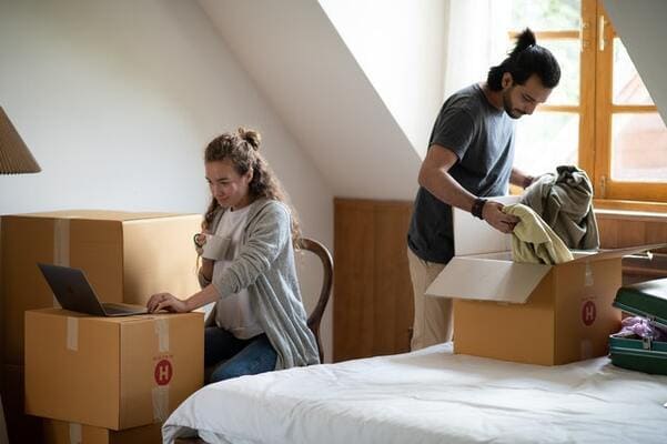 woman typing on laptop while ethnic boyfriend unpacking clothes