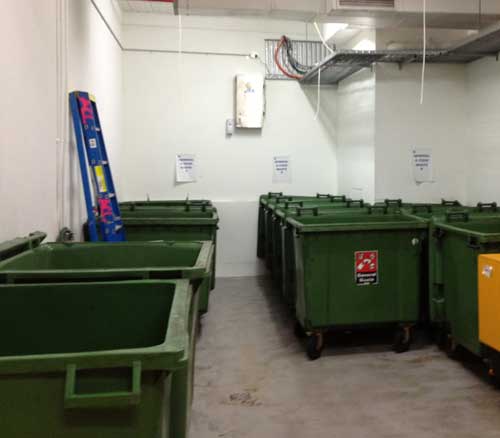 A trash room in a large building with several trash bins