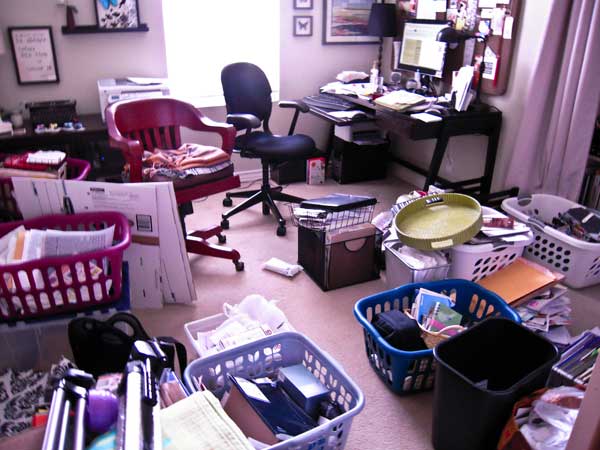 Laundry baskets, boxes, and papers litter the floor of a home office