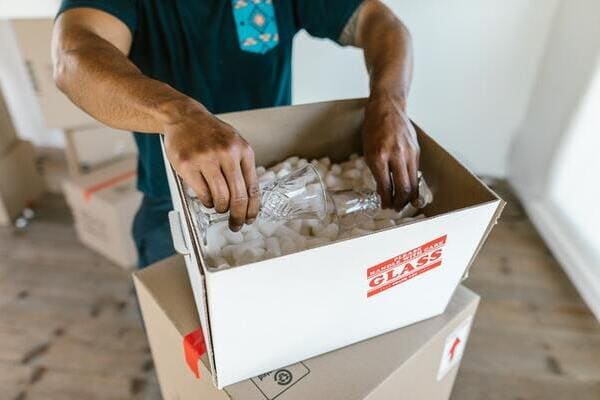 a mover packing glasses into a cardboard box filled with packing peanuts