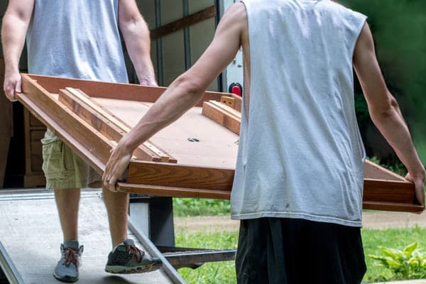 Two men carry furniture up a moving truck ramp