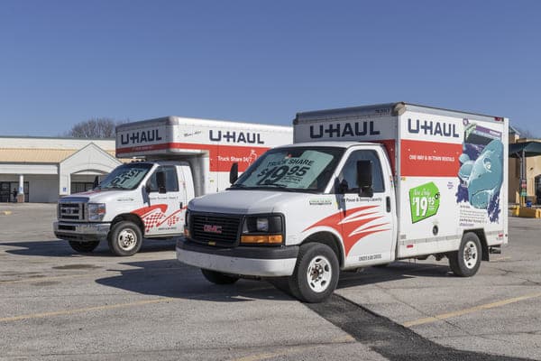 two u-haul moving trucks sit in a parking lot with signs showing them for rent