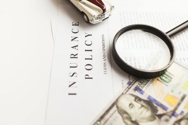 a close-up of an insurance policy with a magnifying glass and hundred dollar bill on top
