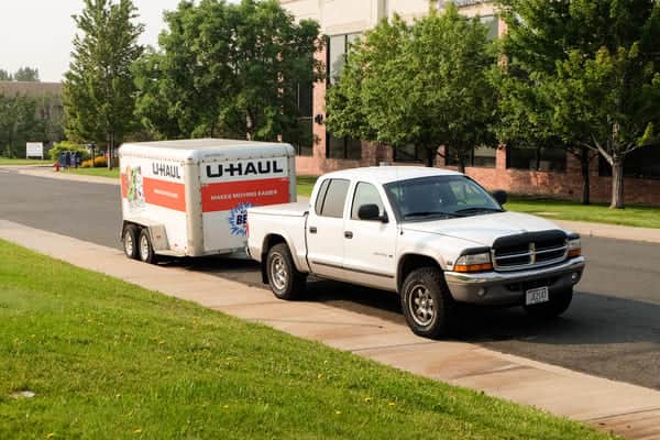 a white pickup truck is towing a U-Haul cargo trailer