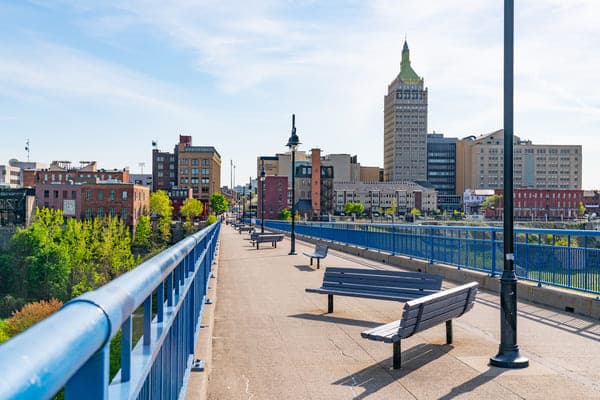 a view of the rochester new york skyline from a sidewalk lined with benches