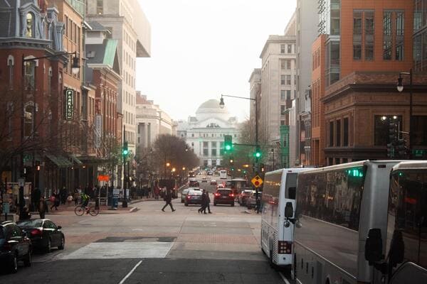 a city street in washington d.c. busy with buses, cars, and people