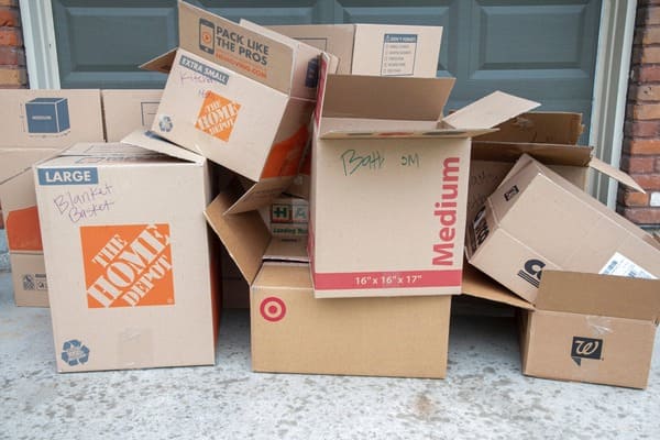 A pile of empty cardboard boxes used for moving sit on a driveway