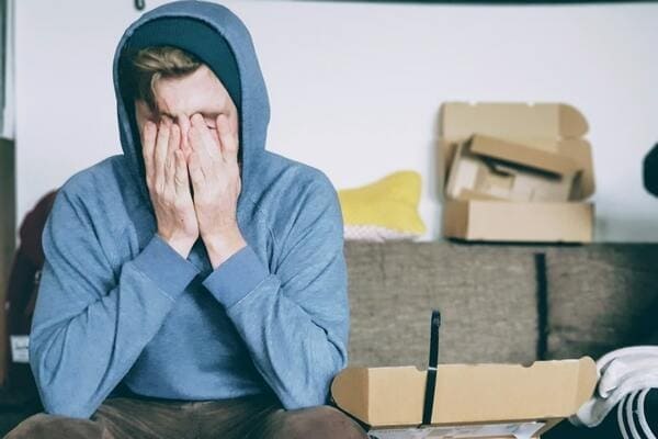 A man rubbing his eyes while sitting in a living room with opened boxes
