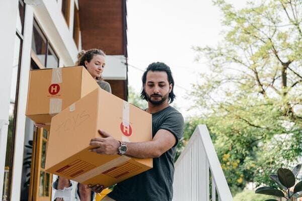 couple carrying boxes on steps while moving out of house