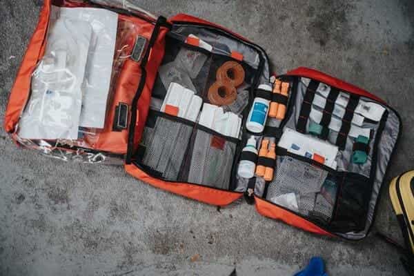 A large red first aid kit is on the ground open displaying various medical items and bandages