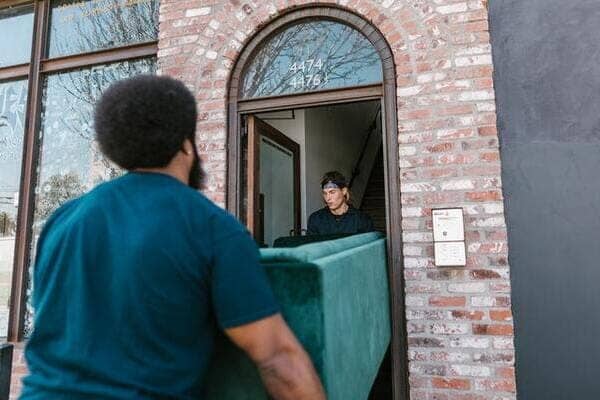 two movers carry a green couch out the front door of a home