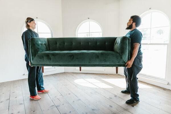 two movers lifting a green couch in an empty room