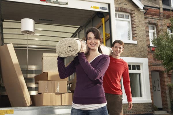 a man and woman have a rug on their shoulders as they unload a moving truck