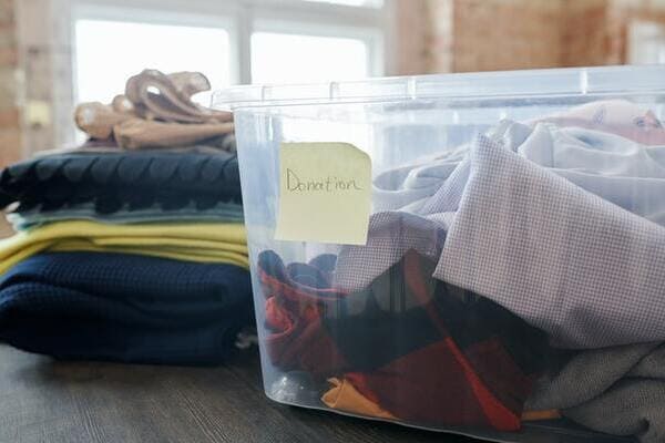 a plastic bin filled with clothes has a yellow sticky that says 'donations' on it