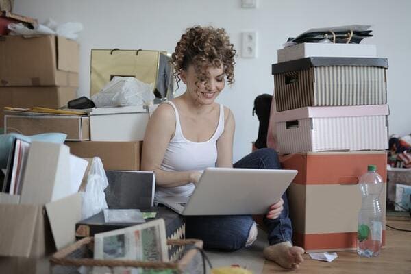 woman using laptop on the floor surrounded by boxes and clutter