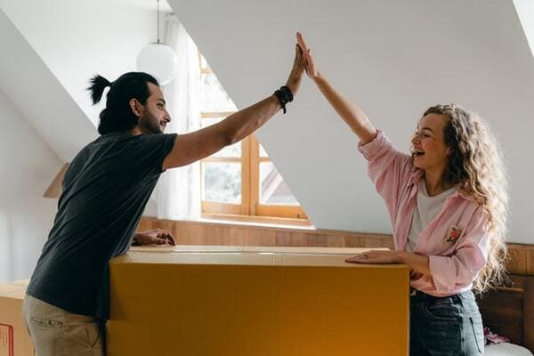 couple in their new apartment high fiving over a cardboard moving box