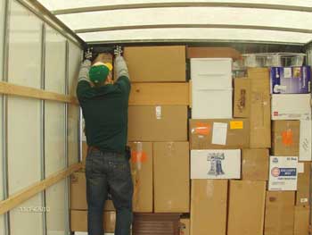 A man places a box on top of other boxes inside of a moving truck
